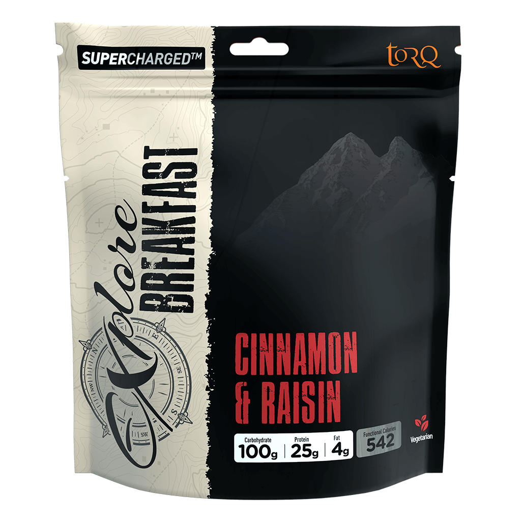 A stand-up pouch of TORQ Adore Breakfast supplement in Cinnamon & Raisin flavor. The packaging is split vertically with a cream-colored top half showing topographic map lines and black script text, and a black bottom half featuring a dark mountain graphic, red product name text, and white nutritional badges.
