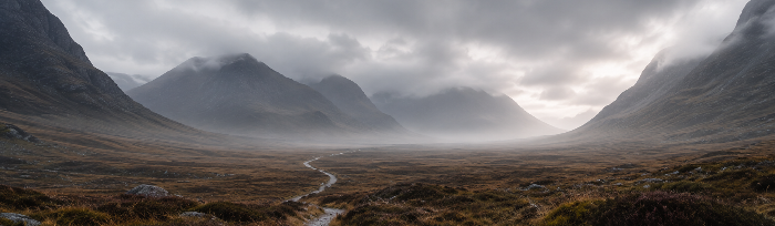 A dramatic mountain landscape with a winding path through a moody valley under heavy gray clouds, with misty peaks in the background.